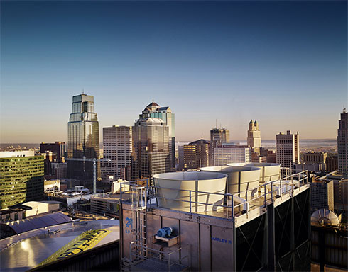 Rooftop induced-draft cooling towers on a downtown building at dusk, city skyline behind